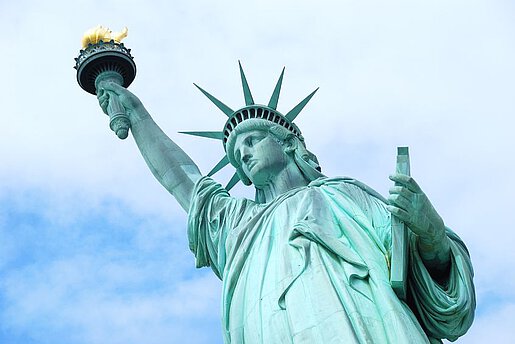 Ansicht der Freiheitsstatue in New York von schräg unten vor einem teilweise bewölkten Himmel