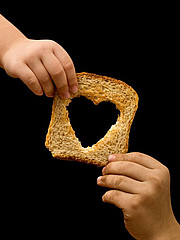 Eine Kinderhand reicht einer anderen Kinderhand eine Toastscheibe, die ein herzförmiges Loch hat.