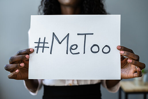 Eine junge Frau hält ein Blatt Papier in die Kamera mit der Aufschrift "#MeToo"