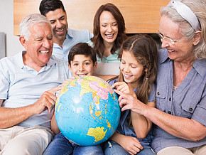 Eine Großfamilie sitzt auf der Couch und alle halten lächelnd einen Globus.