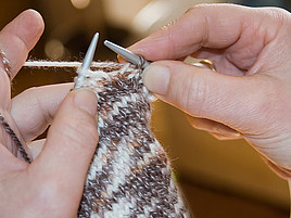 Zwei Hände mit Stricknadeln, die mit Wolle stricken