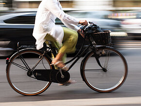 Frau auf Fahrrad mit Auto im Hintergrund