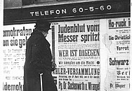 Eine ältere Dame steht vor einem Wahlplakat der Nationalsozialisten im Jahr 1932.