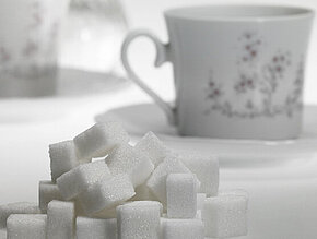 Vor einer Kaffeetasse liegt ein Haufen Zuckerwürfel