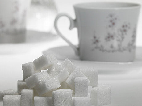 Vor einer Kaffeetasse liegt ein Haufen Zuckerwürfel