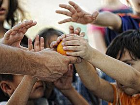 Viele ausgestreckte Hände rund um eine Orange