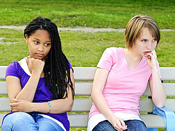 Zwei Teenager sitzen auf einer Bank und wollen nicht miteinander sprechen.