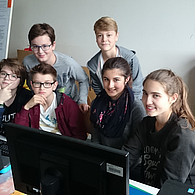 Eine Gruppe Schüler und Schülerinnen vor ihren gemeinsamen Computern.