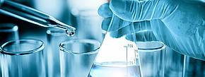 Das Bild zeigt ein Labor und eine menschliche Hand sowie Reagenzgläser