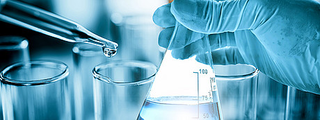 Das Bild zeigt ein Labor und eine menschliche Hand sowie Reagenzgläser