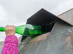Eine Hand wirft eine Flasche in einen Altglaskontainer