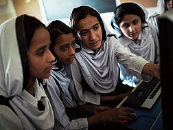Vier Mädchen mit Kopftüchern sitzen vor einem Computerbildschirm