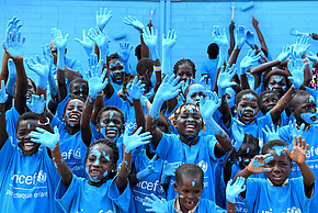 Eine Gruppe Kinder mit blauen UNICEF-T-Shirts halten blau bemalte Händen in die Höhe