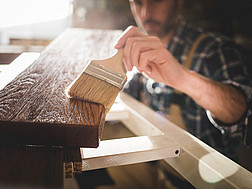 Ein Tischler lackiert ein Holzbrett.