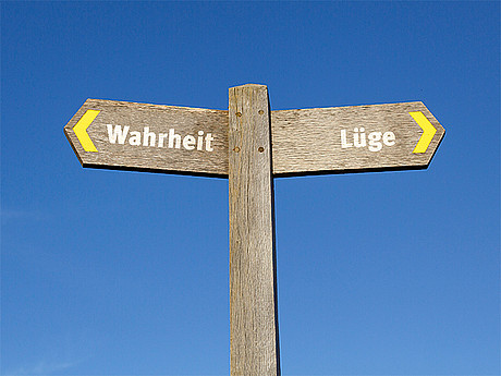 Ein Wegschild mit den beiden Schildern "Wahrheit" und "Lüge", die jeweils in verschiedene Richtungen weisen 