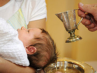Ein Baby wird bei der Taufe mit Weihwasser übergossen.