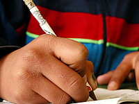 Ein Kind notiert sich etwas mit einem Bleistift in sein Heft.