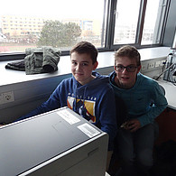 Zwei Schüler vor ihrem gemeinsamen Computer lachen in die Kamera.