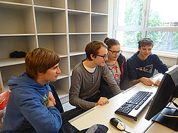 Vier Schüler und Schülerinnen vor ihrem gemeinsamen Computer.