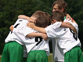 Die Spieler eines Kinderfußball-Teams stehen im Kreis und umarmen sich.
