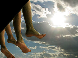 Zwei nach unten baumelnde Füße vor einem Sonnenhimmel