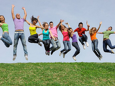 Eine Gruppe von Jugendlichen springt auf einer Wiese gleichzeitig in die Luft.