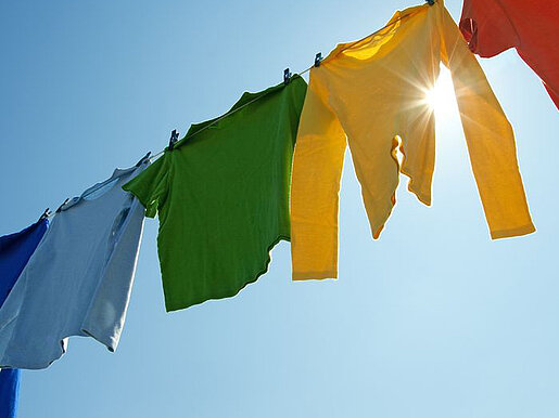 Bunte Kleidungsstücke, die auf einer Wäscheleine unter dem blauen Himmel in der Sonne zum Trocknen hängen