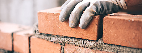 Eine Hand setzt einen Ziegelstein auf eine Mauer, die gerade gebaut wird 