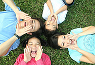 Vier lachende Kinder, die auf einer Wiese liegen von oben fotografiert.