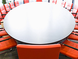 Ein großer Sitzungsraum mit roten Stühlen und einem ovalen Tisch