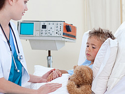 Eine Ärztin untersucht ein Kind, das mit seinem Teddybär in einem Krankenhausbett liegt.