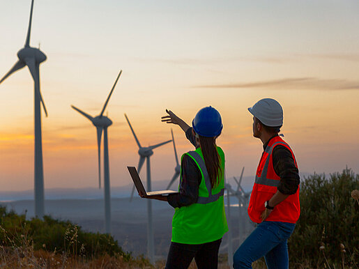 Ingenieurin und Ingenieur stehen vor Windrädern