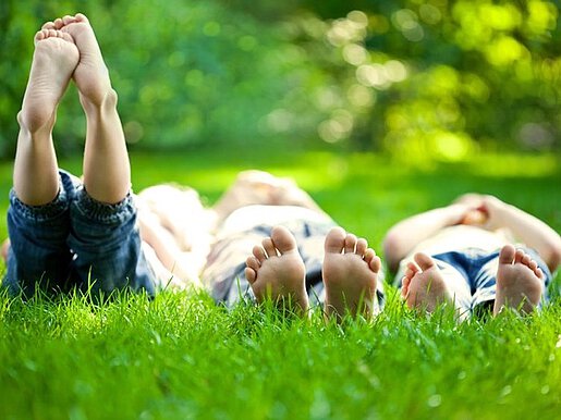 Drei Menschen liegen im grünen Gras, man sieht ihre nackten Füße.