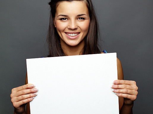 Eine junge Frau vor einem schwarzen Hintergrund hält ein weißes Blatt Papier vor sich.