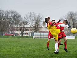 Ein Junge springt mit erhobenem Fuß gegen zwei Spieler der gegnerischen Mannschaft, um den Ball zu bekommen.