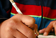 Kinderhand, die mit einem Bleistift in ein Heft schreibt.