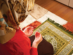 Eine Muslimin mit Kopftuch verrichtet ihr Gebet auf einem Teppich.