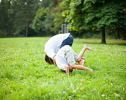 Ein Erwachsener und ein Kind machen auf einer Wiese einen Purzelbaum