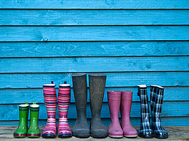 Fünf Paar Gummistiefel in unterschiedlichen Größen und Farben vor einer blauen Holzwand