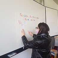 Eine Schülerin klebt ein Post-it an die Tafel