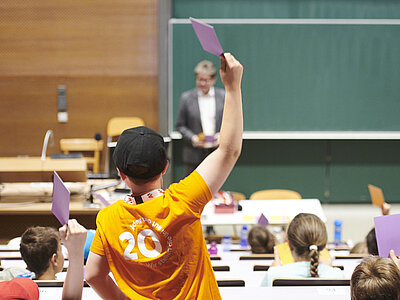 Kinder sitzen im Hörsaal und zeigen auf