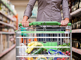 Jemand schiebt einen befüllten Einkaufswagen durch einen Supermarkt.