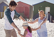 Bild zeigt einen Vater, sein Kind und seine Mutter, die lachend und händehaltend am Strand tanzen.