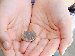 Ein Kind hält eine Euromünze in seinen Händen.