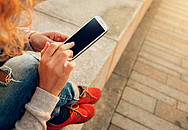 Mädchen auf einer Mauer mit ihrem Smartphone.