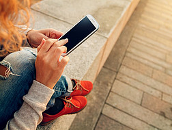 Junge Frau sitzt auf dem Gehsteig mit dem Handy in ihrer Hand