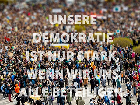 Menschenmasse mit Schriftzug "Unsere Demokratie ist nur stark, wenn wir uns alle beteiligen"