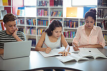 Dire SchülerInnen sitzen in einer Bibliothek und lernen