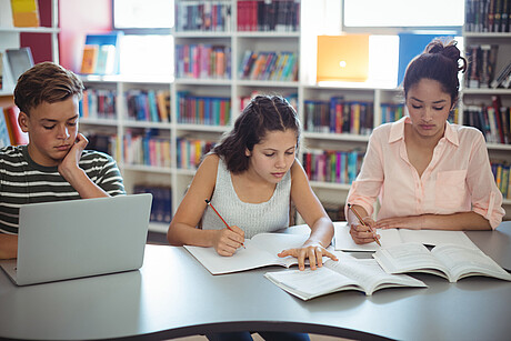 3 SchülerInnen machen in der Bibliothek Hausaufgaben