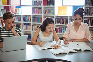 Drei Jugendliche sitzen in einem Raum, vor ihnen Bücher und ein Laptop